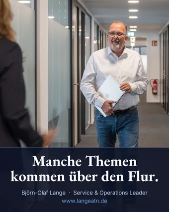 Björn-Olaf Lange im weißen Hemd kommt mit einem Laptop unter dem Arm lächelnd einen hellen Büroflur entlang, links im Vordergrund unscharf eine Kollegin. Im Banderolentext: Manche Themen kommen über den Flur.